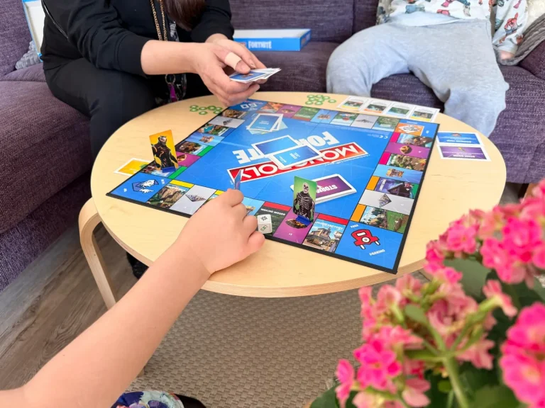 Aikuinen ja nuoria pelaamassa Monopoly Fortnite -lautapeliä olohuoneessa.
